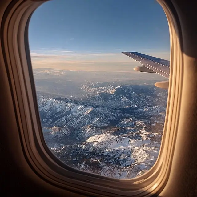 Airplane window seat view above clouds representing global travel services by Ugofly Travels